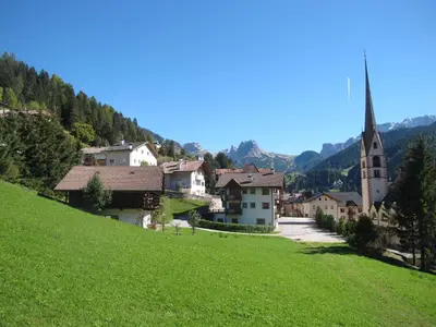 a small village with a church and a green hill at Villa Ula Verda- Apartments Marianna in Santa Cristina in Val Gardena