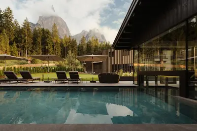 a swimming pool with chairs and mountains in the background at Waldrast - Forestside Living in Siusi
