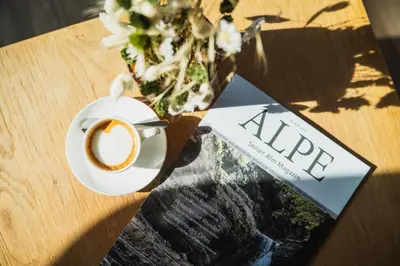 a cup of coffee and a book on a table at Waldrast - Forestside Living in Siusi