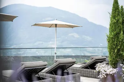 a group of chairs with an umbrella on a patio at Small & Beautiful Hotel Gnaid in Tirolo