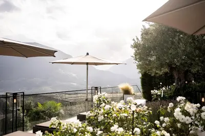 a patio with an umbrella and some flowers at Small & Beautiful Hotel Gnaid in Tirolo