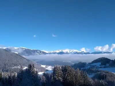 a view of a snowy mountain range with trees and clouds at Natur Apartments Riesen in San Lorenzo di Sebato