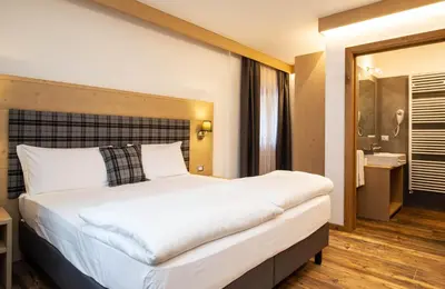 a bedroom with a large white bed and a bathroom at San Martino Mountain Residence in San Martino di Castrozza
