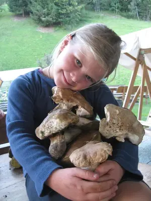 a girl is holding a pile of mushrooms at agriturismo Lüch Picedac in La Valle