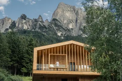 a small wooden house in front of a mountain at Dolomites Nature Hotel Vigilerhof in Siusi