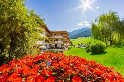 a view of a hotel with red flowers in the foreground at Hotel Castel Oswald von Wolkenstein in Castelrotto