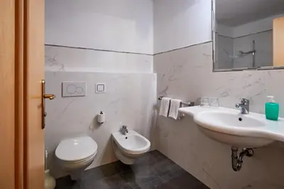 a white bathroom with a toilet and a sink at Alpenhotel Schönwald Superior in Valles