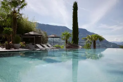 a swimming pool with chairs and trees and a mountain at Feel good Resort Johannis in Tirolo