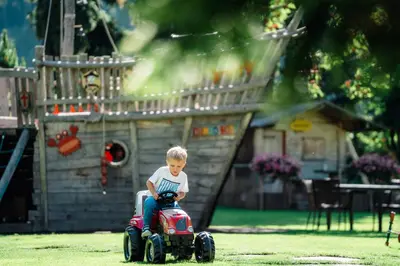a young boy riding a toy car in a yard at Family Hotel Posta in Santa Cristina in Val Gardena