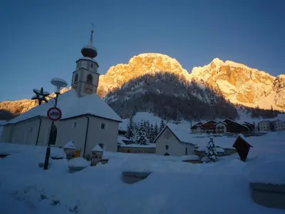 a church in the snow in front of a mountain at Declara B&B and apartaments in Colfosco