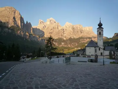 a church with a clock tower in front of a mountain at Declara B&B and apartaments in Colfosco