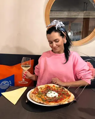 a woman sitting at a table with a pizza at Hotel Wochtla Buam Aktivhotel am Kronplatz mit Sauna in Brunico