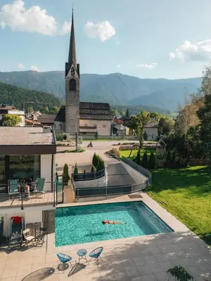a person laying in a swimming pool next to a church at Hotel Wochtla Buam Aktivhotel am Kronplatz mit Sauna in Brunico