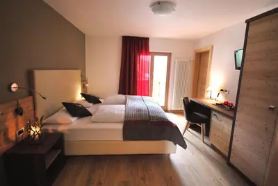 a bedroom with a bed with a desk and a window at Monti Pallidi B&B Apartments in Corvara in Badia