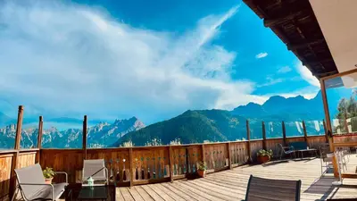 a building with cars parked in a parking lot with mountains at HG Hotel La Caminatha in Val di Zoldo