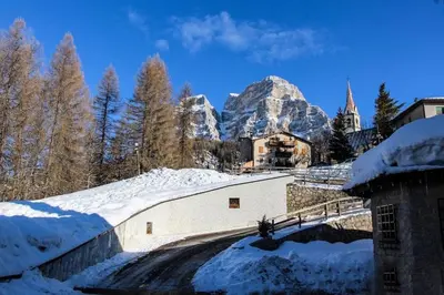 a fence with a view of a house and mountains at HG Hotel La Caminatha in Val di Zoldo