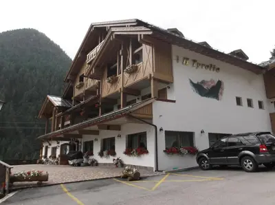 a room with two beds and a desk and a table at Hotel Tyrolia in Malga Ciapela
