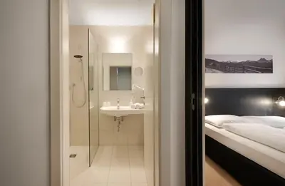 a bathroom with a shower and a sink next to a bed at Hotel Tirolerhof in Rodengo