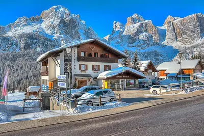 a building with cars parked in front of a mountain at Garnì Bel Air in Colfosco