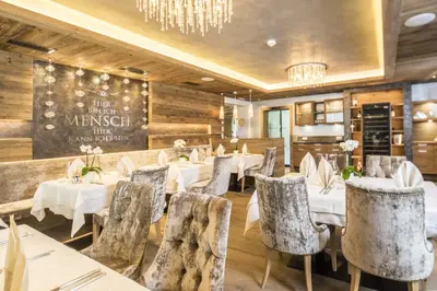 a restaurant with tables and chairs and a chandelier at Alpin Hotel Sonnblick in Perca