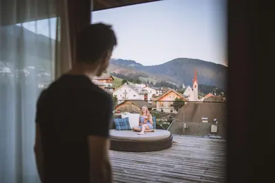 a woman sitting on a bed on a balcony at Alpin Hotel Sonnblick in Perca