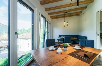 a dining room with a wooden table and large windows at Haus Herta B&B in Nova Levante