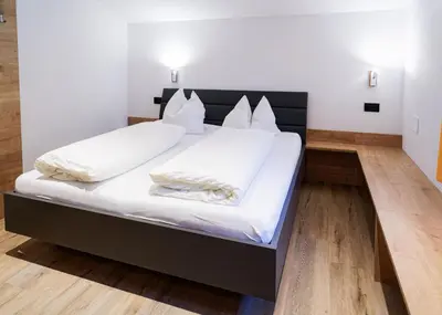 a bedroom with a large bed with white sheets at Haus Herta B&B in Nova Levante