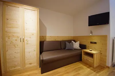 a living room with a couch and a tv on the wall at Garnì Tofana in Corvara in Badia