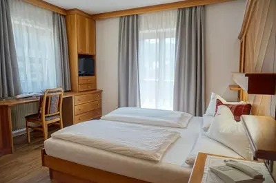 a hotel room with a bed and a desk and window at Garnì Tofana in Corvara in Badia
