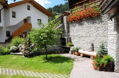 a garden with a bench and a brick wall with flowers at Ciasa Confolia in Corvara in Badia