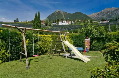 a swing set in a garden with mountains in the background at Residence Neuhof in Tirolo