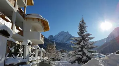 a snow covered building with a christmas tree in front of a mountain at Hotel Cesa Tyrol in Canazei