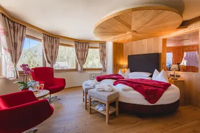 a bedroom with a large bed and red chairs at Hotel Cesa Tyrol in Canazei
