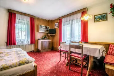 a room with a table and a bed and red curtains at Apartments Fiordalisi in Colfosco