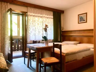 a bedroom with a bed and a table and a window at Apartments Fiordalisi in Colfosco