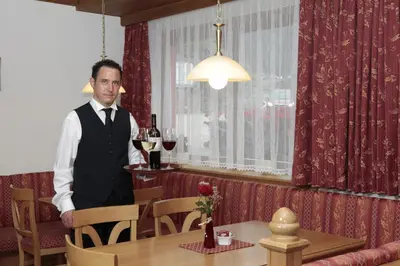 a man in a vest and tie standing next to a table at Hotel Alpino Plan in Selva di Val Gardena