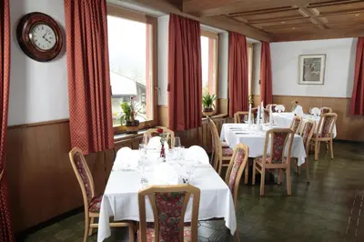 a restaurant with white tables and chairs and a clock at Hotel Alpino Plan in Selva di Val Gardena