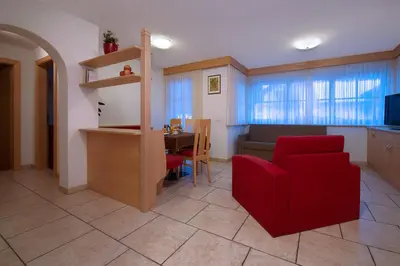 a living room with a red chair and a table at Appartamenti Villa Olympia in Corvara in Badia