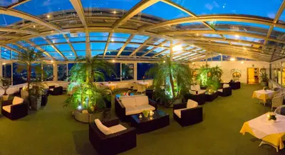 an indoor restaurant with tables and chairs and plants at Panorama Vital Hotel Rimmele in Tirolo