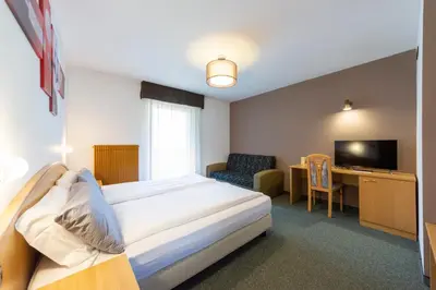 a hotel room with a bed and a desk and a television at Flos Hotel in Moena