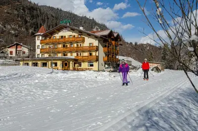 two people on skis in the snow in front of a lodge at Flos Hotel in Moena