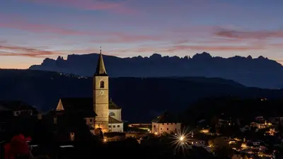 a church with a steeple at night with mountains in the background at Reiterhof Edelweiss in San Genesio Atesino