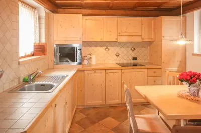 a kitchen with wooden cabinets and a sink and a table at Tabià Elisa in Campitello di Fassa