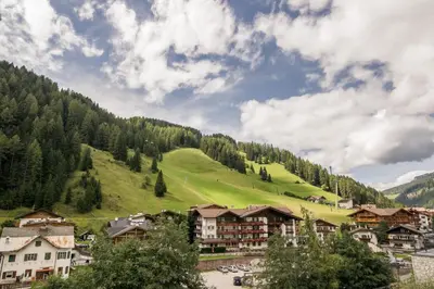 a village in the mountains with a green hill at Casa Matie in Selva di Val Gardena