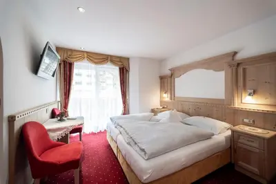 a bedroom with a large bed and a red chair at Garni B&B Schenk in Selva di Val Gardena