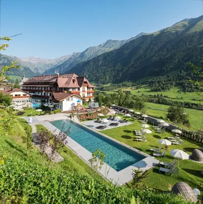 a resort with a pool and mountains in the background at Hotel Sonklarhof in Ridanna