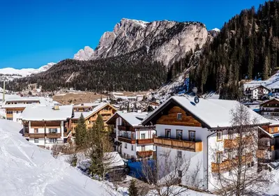 a house in the snow with mountains in the background at Garni Lanzinger in Selva di Val Gardena