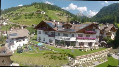 a large building on a green hill with a house at Hotel Pra Tlusel in Selva di Val Gardena