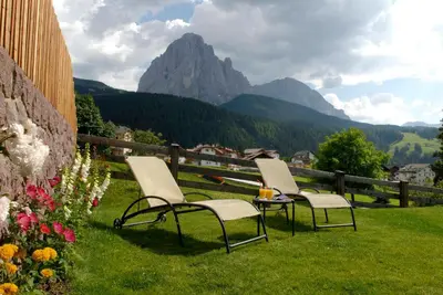 two chairs and a table in the grass with a mountain at Hotel Pra Tlusel in Selva di Val Gardena
