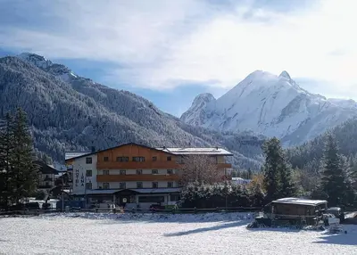 a hotel with cars parked in front of a mountain at Dolomiten Hotel Irma in Canazei
